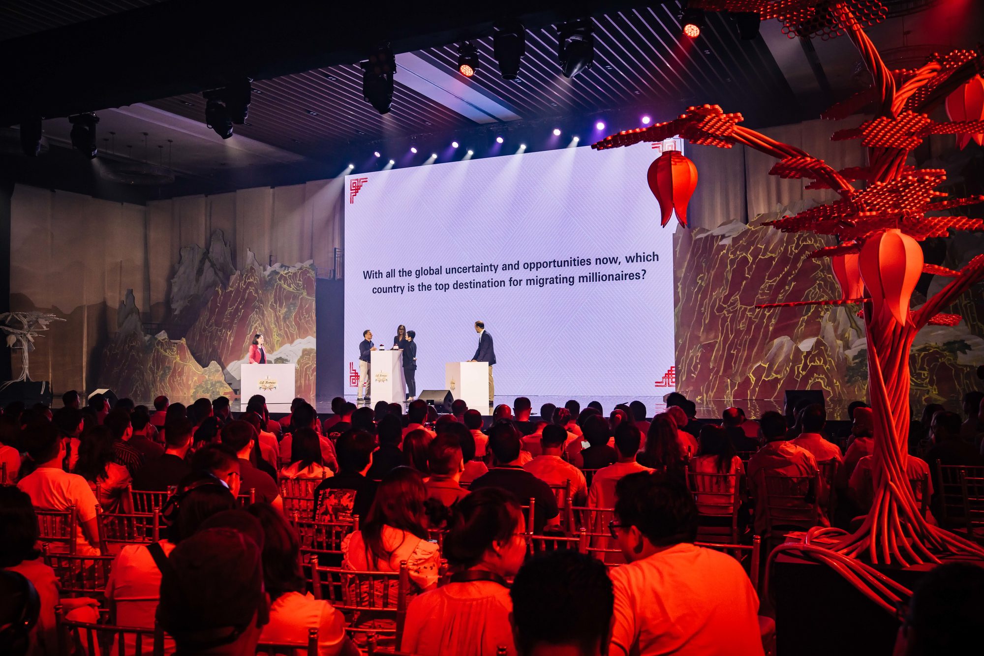 A full plenary session in progress, audience seated, stage, screen and scenic build
