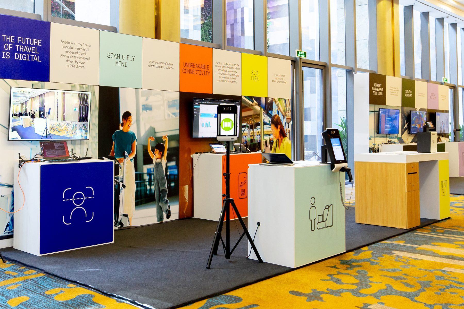 Full run of exhibition demo pods along the branded wall with self-service kiosks