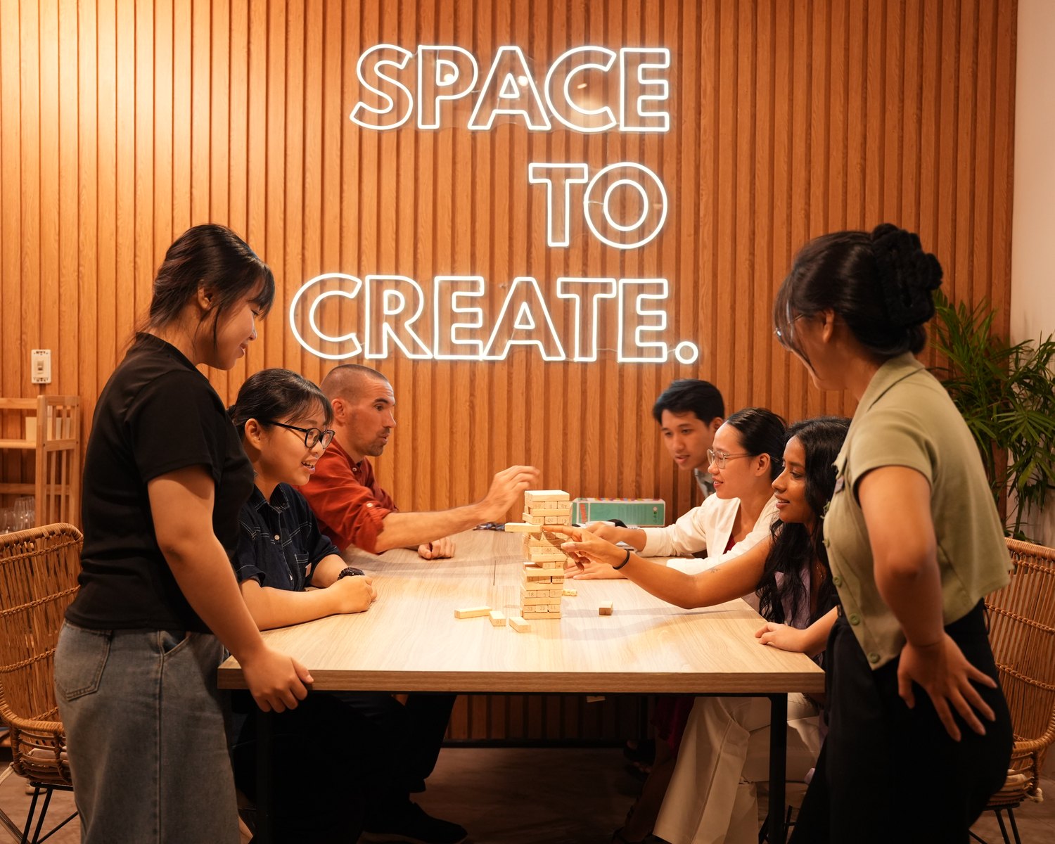 The iMAGINE Events Asia team around the games table at the Da Nang office, under the studio's SPACE TO CREATE neon sign