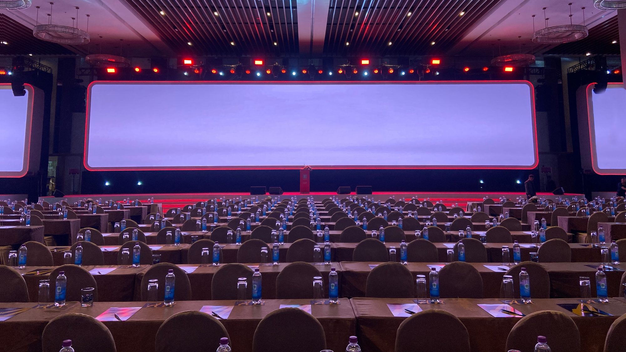 A large LED screen lit above rows of empty conference chairs